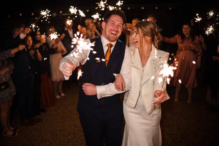 Wedding photograph by Sky Photography — a couple laugh as they walk out through a guard of sparklers held by their guests